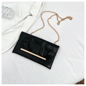 Détail d'une pochette plissée noir brillant avec chaîne et barre métallique dorées