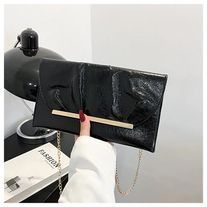 Détail du sac enveloppe noir en cuir verni plissé avec chaîne dorée et garniture métal