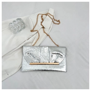 Détail du sac à main plissé argenté avec chaîne en métal doré et barre dorée décorative
