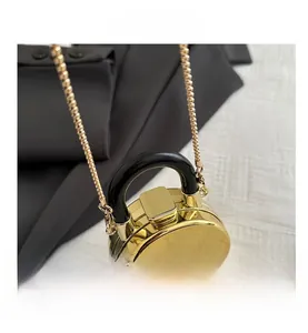 Detail of a mini round gold metallic purse with polished finish and black handle