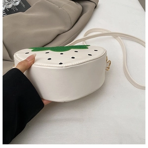 Détail du sac bandoulière en forme de fraise avec feuille verte et boucle dorée chic