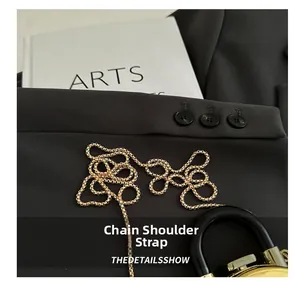 Detailed close-up of a glossy gold chain shoulder strap with woven ring design on black fabric