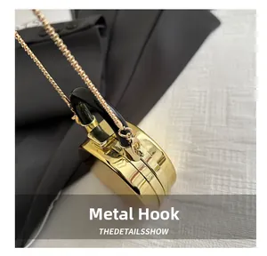 Detail of gold hard shell evening bag with black curved handle and fine metal chain strap