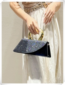 Detail of silver rhinestone flap with chunky gold handle on a black leather crossbody bag