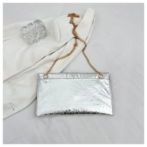Détail d'une pochette argentée plissée avec chaîne dorée sur fond de tissu blanc