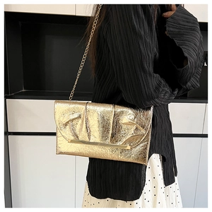 Détail d'un sac à bandoulière doré plissé avec chaîne fine en or et bordure métallique