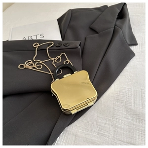 Close-up of mini gold metallic box bag with black curved handle and delicate gold chain