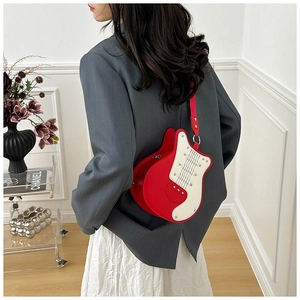 Detail of creative red guitar-shaped crossbody bag worn over a grey blazer and white skirt