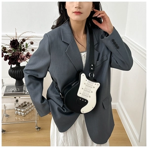 Creative guitar-shaped crossbody bag with rivet details worn by model in casual chic outfit
