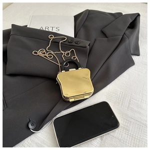 Macro detail of toast-shaped gold mini acrylic box bag on a grey suit jacket