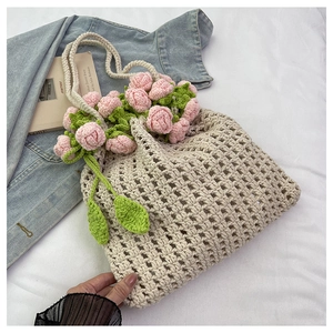 Close-up of hand-woven beige tote bag with crochet pink roses and green leaves