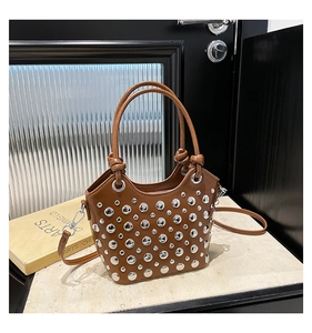 Detailed view of brown bucket bag with silver rivets, dual handles and marble background