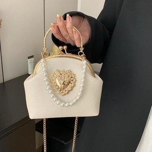 Cream pearl crossbody bag with gold heart clasp and metal handle in elegant setting