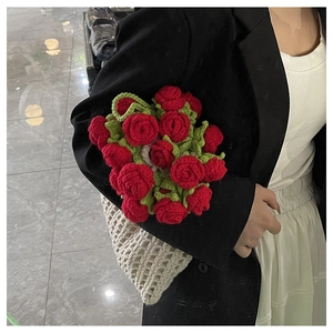 Close-up of handmade crochet red rose bouquet in white mesh knitted bag with green leaves