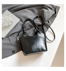 Detail of glossy black leather tote bag with silver metal rings on a grey blazer background