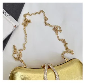 Close-up of gold glossy evening bag with brushed texture and diamond-encrusted drop clasp