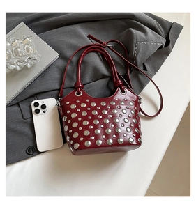 Detail of red bucket bag with silver studs and adjustable strap on a grey suit jacket