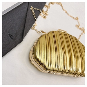 Close-up of golden shell clutch with vertical pleat texture and delicate chain strap