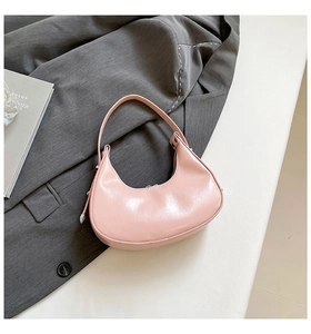 Detail view of a pink crescent-shaped leather handbag against a stylish grey blazer