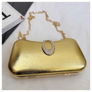Macro view of golden hard shell evening clutch with textured metal surface and diamond buckle