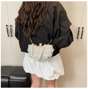 Detailed shot of white lace evening bag with pearl handle and metal chain on a model