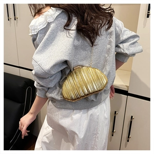 Detail of a golden shell-shaped chain bag with metallic pleated texture on a model