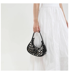 Detail of silver rivets on a black hobo bag held by a model in a white dress