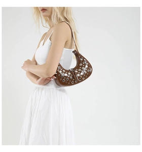Detail of a brown leather hobo bag featuring silver rivets and a modern Y2K industrial style
