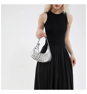 Detail of silver crescent Hobo bag with metallic studs held by a model in black