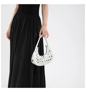 Close-up of white crescent shoulder bag with silver eyelet studs on black dress