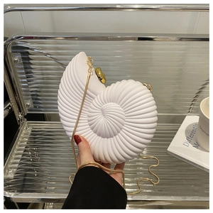 Detail of white acrylic conch shell clutch bag with gold chain strap held by hand
