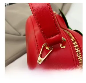 Détail du crochet en métal doré et de la bandoulière en cuir rouge cousue sur le sac fraise