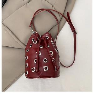 Détail du sac seau bordeaux avec œillets argentés et rivets sur un blazer beige