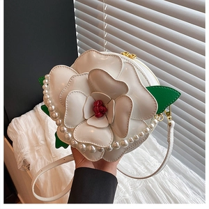 Detail of camellia shaped handbag featuring pearl trim and green leaf accents