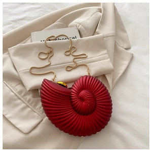 Detail of red conch-shaped acrylic crossbody bag with a golden snake chain strap