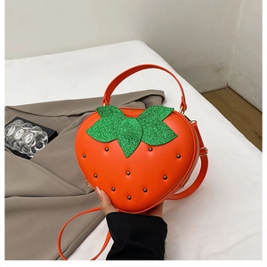 Détail du sac bandoulière fraise avec design de feuille verte et clous métalliques