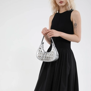 Silver rivet half-moon shoulder bag in metallic leather worn by model on white background