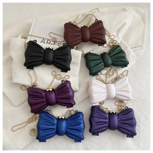 Vue de dessus de mini-sacs nœuds colorés avec chaînes dorées sur un tissu blanc doux