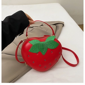 Détail d'un sac à main rouge en forme de fraise avec feuilles vertes et clous dorés