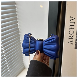 Détail du sac de soirée bleu en forme de nœud avec chaîne dorée et texture mate