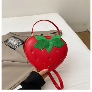 Détail d'un sac à main fraise rouge avec feuilles vertes scintillantes et clous noirs