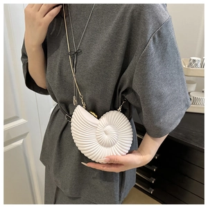 Detailed view of white shell-shaped acrylic clutch with elegant gold chain strap