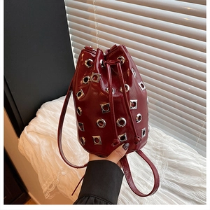 Détail du sac seau bordeaux en cuir verni avec œillets métalliques et fermeture à cordon