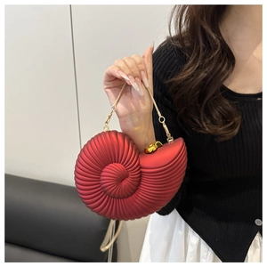 Detail of red conch shell clutch bag with gold heart clasp and metal chain strap