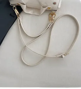 Detail of adjustable off-white leather strap and golden metal clasp on women's bag