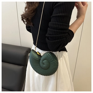 Deep green nautilus shaped crossbody bag with matte texture and gold chain on model