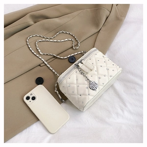 Detail of quilted beige crossbody bag with sparkling rhinestones and metal flower charm