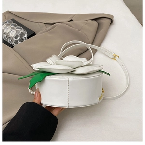 Detailed view of 3D white flower with green leaves on round crossbody bag with pearls