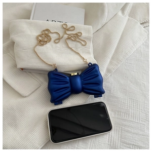 Détail du mini sac nœud bleu marine avec chaîne dorée comparé à la taille d'un téléphone