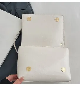 Detail of cream crackle leather handbag with dual gold magnetic clasps on textured surface